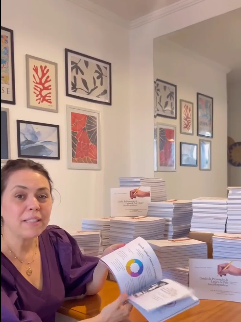 Elaine Ianni mostrando o Guia aberto na página da Mandala da Prevenção, com pilhas de exemplares ao fundo